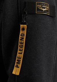Tissu noir avec une étiquette PME Legend jaune et une sangle jaune assortie avec un texte noir, attachée par un fermoir en métal noir.