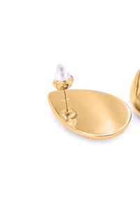 Orecchini color oro con una forma ovale liscia. Comprendono un retro in plastica bianca e una finitura lucida che riflette efficacemente la luce.