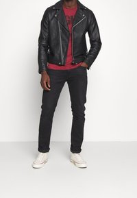 Chaqueta de cuero negra de motorista con cremalleras plateadas, camiseta gráfica roja, jeans oscuros y zapatillas blancas. Atuendo casual con texturas suaves.