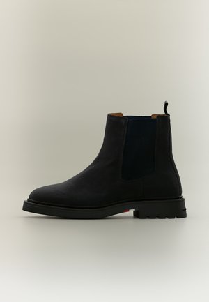 Botte Chelsea en cuir noir avec panneaux latéraux élastiques, languette à l’arrière et semelle épaisse en caoutchouc avec crampons robustes.