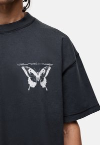 Zwart oversized t-shirt met een grote witte vlinderafbeelding en de tekst "Good For Nothing" in cursief boven het ontwerp.