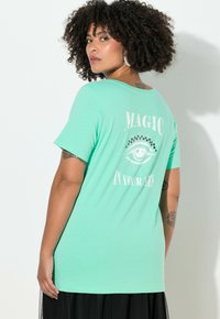 Tričko v mátově zelené barvě s volnějším střihem, na zádech s potiskem oka a nápisem „MAGIE VE TVÝCH OČÍCH".