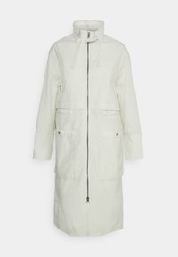 Dlouhý krémový kabát s vysokým límcem, předním zipem, dvěma velkými předními kapsami se snap knoflíky a nastavitelnými popruhy na krk.