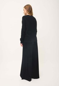 Pull en laine noir avec un col rond et des manches longues, associé à un pantalon noir en velours à jambes larges avec une texture douce.