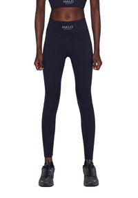 Marineblauwe high-waisted leggings gemaakt van rekbaar materiaal, met een zachte textuur en een HALO-logo op de tailleband, gecombineerd met zwarte sportschoenen.