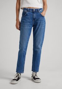 Blå denimjeans med rak passform, fem fickor, knapp- och dragkedjestängning och subtila blekningar, i kombination med svarta sneakers.