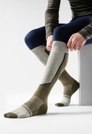 Calcetines hasta la rodilla con un diseño texturizado, que presentan una combinación de colores en verde oliva y crema, y sutiles patrones geométricos.