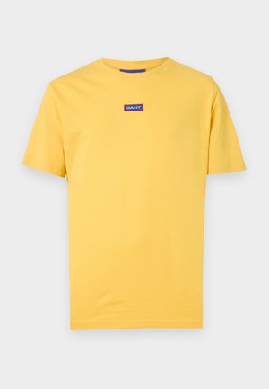 T-shirt jaune à manches courtes avec col rond, comportant un petit patch logo GANT bleu et blanc centré sur la poitrine.