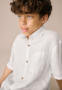Weißes Leinen-Hemd mit kurzen Ärmeln, durchgehendem Knopfverschluss und Brusttasche. Verfügt über Holzknöpfe und eine strukturierte Stoffoberfläche.