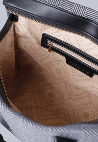 Interno di una borsa nera e grigia con una tasca con zip liscia, foderato in beige con un motivo a logo ripetuto del marchio e hardware della zip in oro.