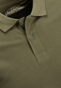 Olivgrünes Polohemd aus strukturiertem Stoff, mit klassischem Kragen, zwei Knöpfen und dezentem Markenlogo innen am Kragen.