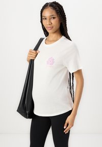 Hvit kortermet t-skjorte laget av mykt stoff, med et rosa grafisk design på brystet. Kombinert med svarte tights og en svart veske.