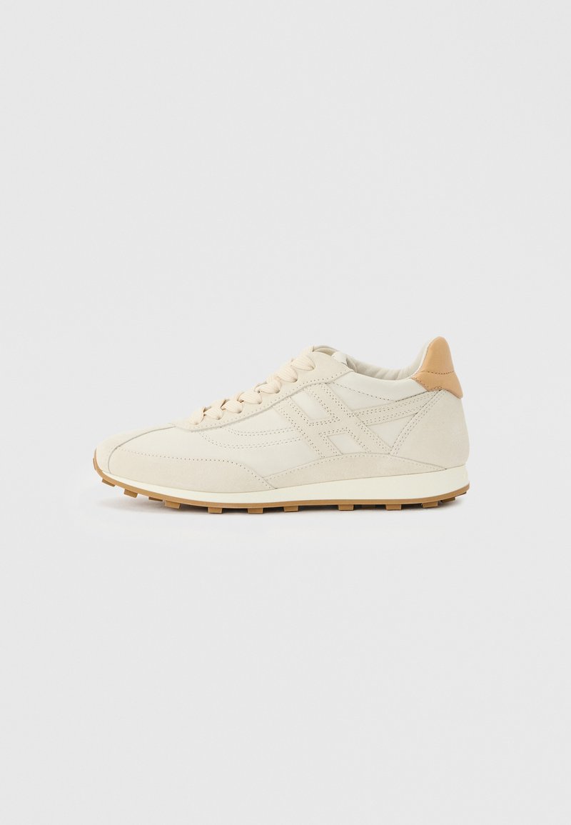 Μπεζ αθλητικό παπούτσι χαμηλού τύπου με ραμμένες λεπτομέρειες, ταμπά ταμπάκι στη φτέρνα, δέσιμο με κορδόνια μπροστά και αυλακωτή σόλα από καουτσούκ σε απλό ανοιχτό φόντο.