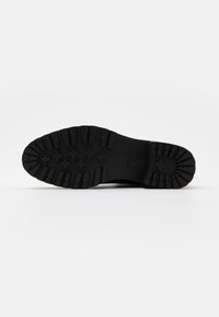 Suela de bota de goma negra con un patrón de textura, que presenta agarres rectangulares y en forma de cruz para mejorar la tracción y la durabilidad.