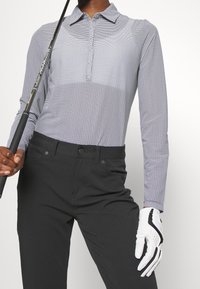 Långärmad pikétröja i ljusgrått med ett geometriskt mönster, med krage, knapplist och i sällskap av svarta byxor och en golfklubba.