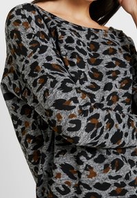 Maglione grigio a stampa leopardata con motivi neri e marroni, scollo ampio e tessuto morbido e testurizzato. Le maniche sono larghe.