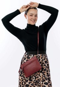 Bolso cruzado burdeos con dos compartimentos con cremallera, hecho de cuero texturizado, colgado de una correa al hombro sobre una falda de estampado de leopardo.