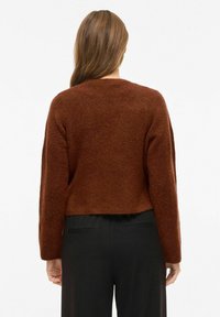 Brązowy, puszysty krótki sweter z długimi rękawami i okrągłym dekoltem, zestawiony z czarnymi spodniami, pokazany od tyłu.