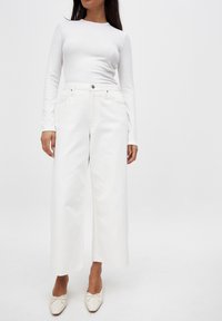 Witte lange mouw top met een ribbelstructuur, gecombineerd met hoge witte wijde jeans met voorzakken en zilveren hardwaredetails.
