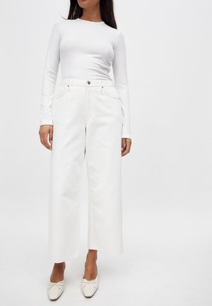 Witte lange mouw top met een ribbelstructuur, gecombineerd met hoge witte wijde jeans met voorzakken en zilveren hardwaredetails.