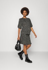 Vestido de padrão de Leopardo com mangas bufantes, saia até ao joelho, botins pretos e uma mala texturada preta. O tecido parece suave e cai bem.