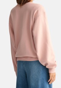 Sweat-shirt oversize rose avec épaules tombantes et poignets côtelés, associé à un jean bleu ample. Tissu doux avec une texture lisse.