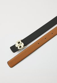 Mustad ja pruuni nahast vööd, üks kuldse kahe B-klambriga, millel on siledad ja tekstureeritud pinnad ning mitmed reguleerimisaugud.