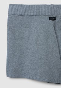 Pantaloni corti grigi in maglia con vita a costine, dotati di un'etichetta con la dicitura "ZERO WASTE DESIGN". Texture liscia, vestibilità leggermente ampia.