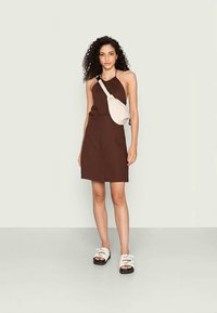 Vestido castanho com alças, com um corpete justo e saia rodada. Combinado com sandálias brancas com tiras largas e uma bolsa cruzada bege.