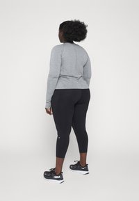 Grey long-sleeve top and black leggings. Fabric textures are smooth. Black athletic shoes with white accents. Back view, facing away.