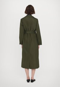Olijfgroene trenchcoat met lange mouwen, een ceintuur in de taille en een lengte tot halverwege de kuit, met een split aan de achterkant en een klassieke kraag.