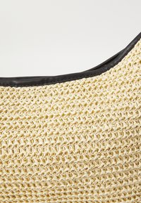 Kudottu olkilaukku, jossa on teksturoitu beige runko ja sileä musta nahkareuna ylhäällä.