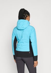 Blå isoleret jakke med hætte, der har sorte sidepaneler og en quiltet tekstur. Slim-fit design, der er velegnet til udendørs aktiviteter.