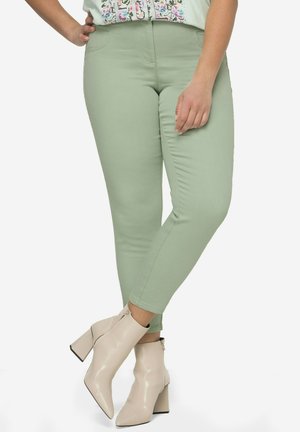 Světle zelené skinny džíny vyrobené z elastické látky, s vysokým pasem a hladkou texturou, v kombinaci se světle béžovými kotníkovými botami.