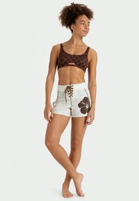 Hnedý vzorovaný crop top a biele šortky s veľkým hnedým kvetinovým dizajnom, s šnurovaním vpredu a hladkým materiálovým povrchom.