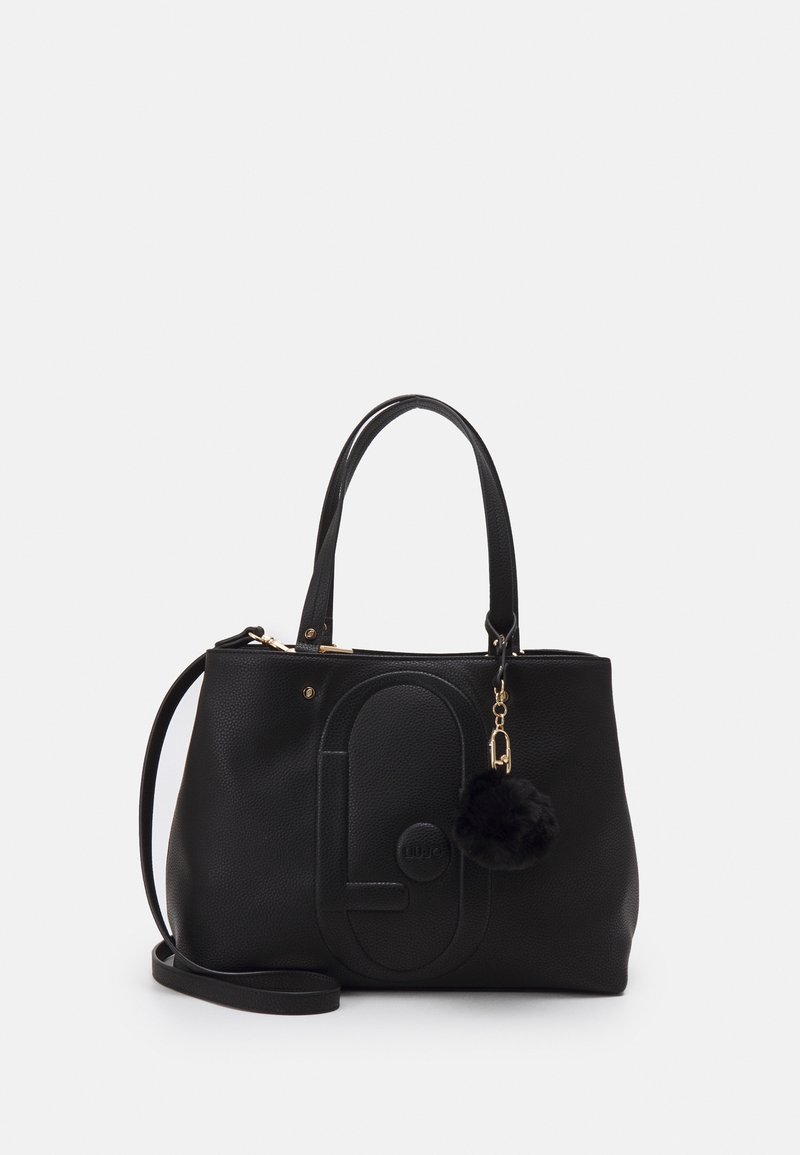 Sac à main noir texturé avec poignées supérieures et bandoulière amovible. Présente un logo et un pompon noir en guise de charme.