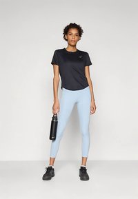 Maglietta sportiva nera a maniche corte, leggings azzurri, scarpe da ginnastica nere, tiene in mano una bottiglia d'acqua nera con logo bianco. Tessuto liscio, design aderente.