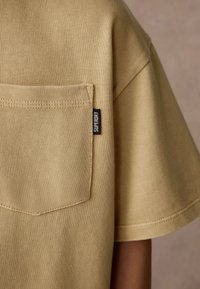 Khaki kortärmad skjorta med ribbad struktur, med en bakficka och en svart "Superdry"-etikett på sidsömmen.