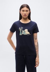 Μπλούζα από βαμβάκι σε ναυτικό μπλε χρώμα με γραφικό που απεικονίζει έναν σκύλο, μια γλάστρα και μπότες γαλότσες. Κοντά μανίκια, στρογγυλή λαιμόκοψη και άνετη εφαρμογή.