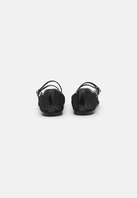 Sandales noires avec un design en maille texturée, des lanières fines et un panneau arrière lisse. Semelle plate avec un minimum de matériel.