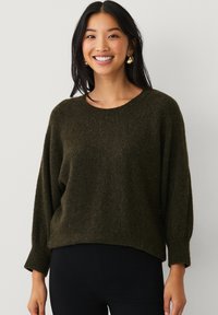 Pull en maille texturée vert foncé avec une coupe décontractée, un col rond et de longues manches légèrement bouffantes. Détails d'accent lisses présents.