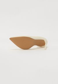 Beżowy but na wysokim obcasie z ostrym noskiem, gładkim wierzchem i jasnobrązową fakturowaną podeszwą. Posiada smukły obcas w stylu stiletto.