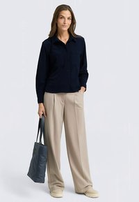 Navy ribbed button-up shirt paired with beige wide-leg trousers and a grey tote bag; model wearing cream slip-on shoes.