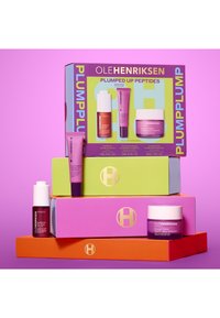 Vier gestapelte Kisten in leuchtenden Farben: orange, pink, grün und lila. Enthält Hautpflegeprodukte mit unterschiedlichen Formen und Etiketten.