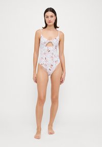 Maillot de bain une pièce blanc avec un motif floral dans des couleurs pastel, présentant des bretelles fines et un design décolleté à l'avant.