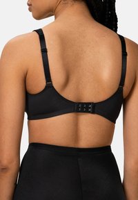 Černá podprsenka s nastavitelnými ramínky, háčkovým zapínáním na zádech a hladkým povrchem. Hodí se k černým kalhotám s vysokým pasem.