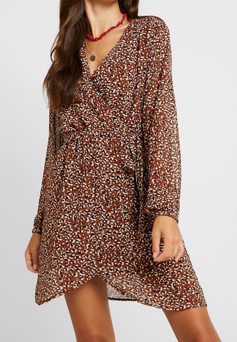 Robe portefeuille marron en tissu léger avec un imprimé animalier dispersé en crème et bleu sarcelle. Manches longues avec poignets froncés et texture douce.