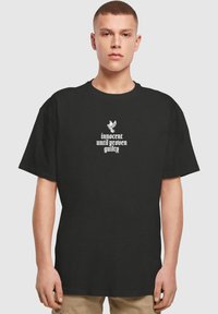 Schwarzes Baumwoll-T-Shirt mit kurzen Ärmeln, Rundhalsausschnitt und einem grafischen Design mit dem Text „unschuldig bis zur Schuldüberprüfung“ in Weiß.