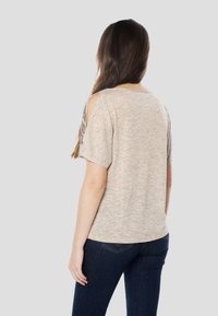 Lichtbeige top met korte mouwen en uitsnijding bij de schouders, textuurstof en een losse pasvorm, gecombineerd met donkerblauwe spijkerbroek.