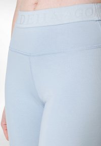 Ljusblå leggings i mjukt, elastiskt material. Har ett brett midjeband med präglad text och förstärkt sömnad längs sömmarna.